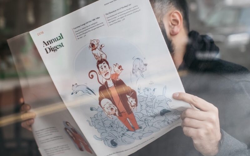 Persoană care citește o revistă cu o ilustrație editorială a cuiva într-o grămadă de pisici pe copertă