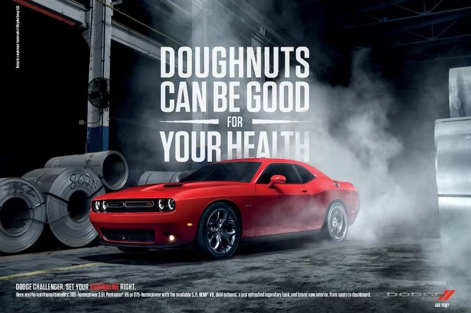 赤いダッジ チャレンジャーが工場に座っており、その後ろには大きな太字で「ドーナツは健康に良い」という言葉が書かれています。