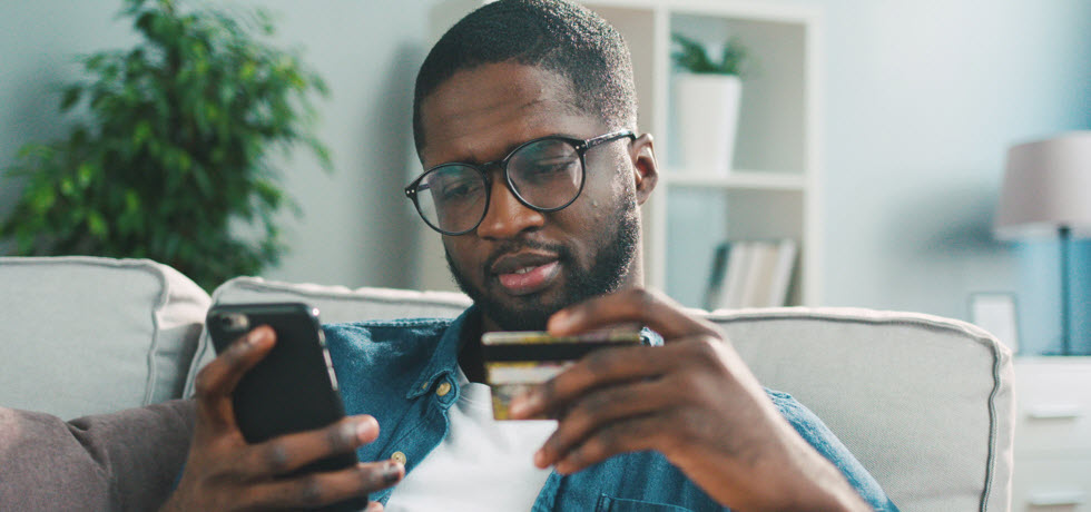 メガネをかけた若い男性が自宅でスマートフォンを使用してクレジットカードでオンラインショッピングをする