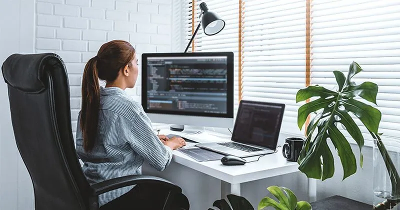 Une jeune femme est assise au bureau et optimise un site Web sur son ordinateur portable.