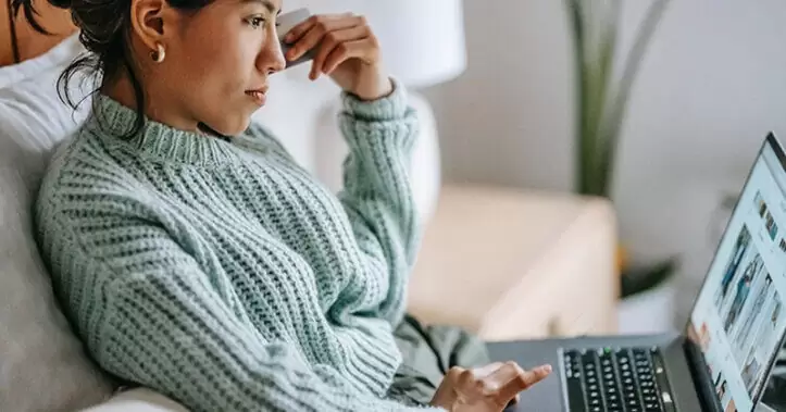 امرأة تجلس على الأريكة وتتصفح المتجر عبر الإنترنت على جهاز الكمبيوتر المحمول الخاص بها.