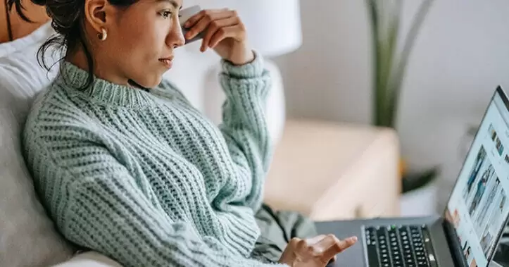 Wanita duduk di sofa menelusuri toko online di laptopnya.