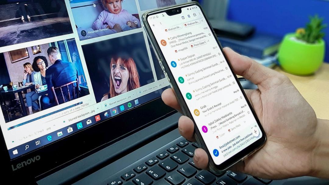 dizüstü bilgisayarın yanında telefonu tutan kişi